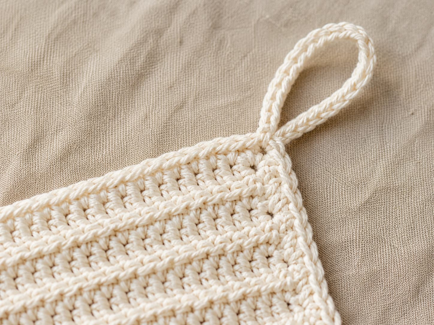 Chain-12 hanging loop and slip stitch join at the corner of a finished cream cotton crochet dishcloth.