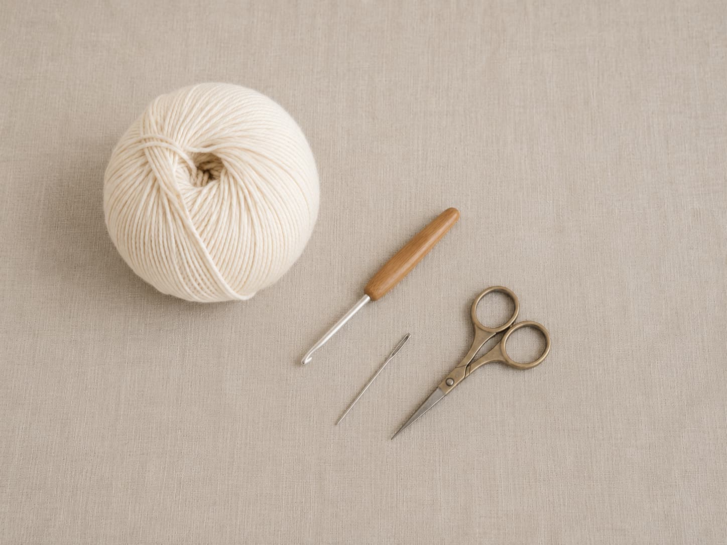 Cream cotton yarn, 5.0 mm crochet hook, small scissors, and tapestry needle arranged on natural linen.