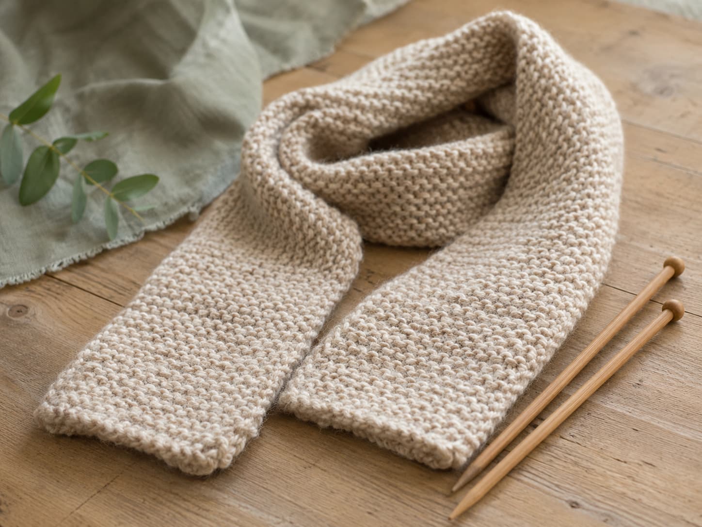Illustration of a beginner garter stitch scarf beside wooden knitting needles.