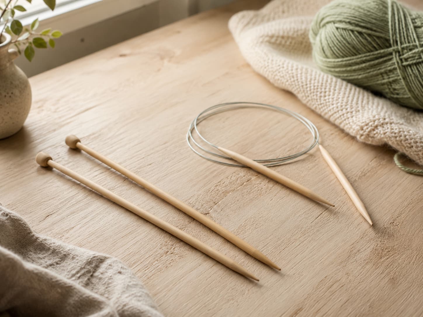 Illustration of straight and circular knitting needles displayed with soft yarn for a beginner guide.