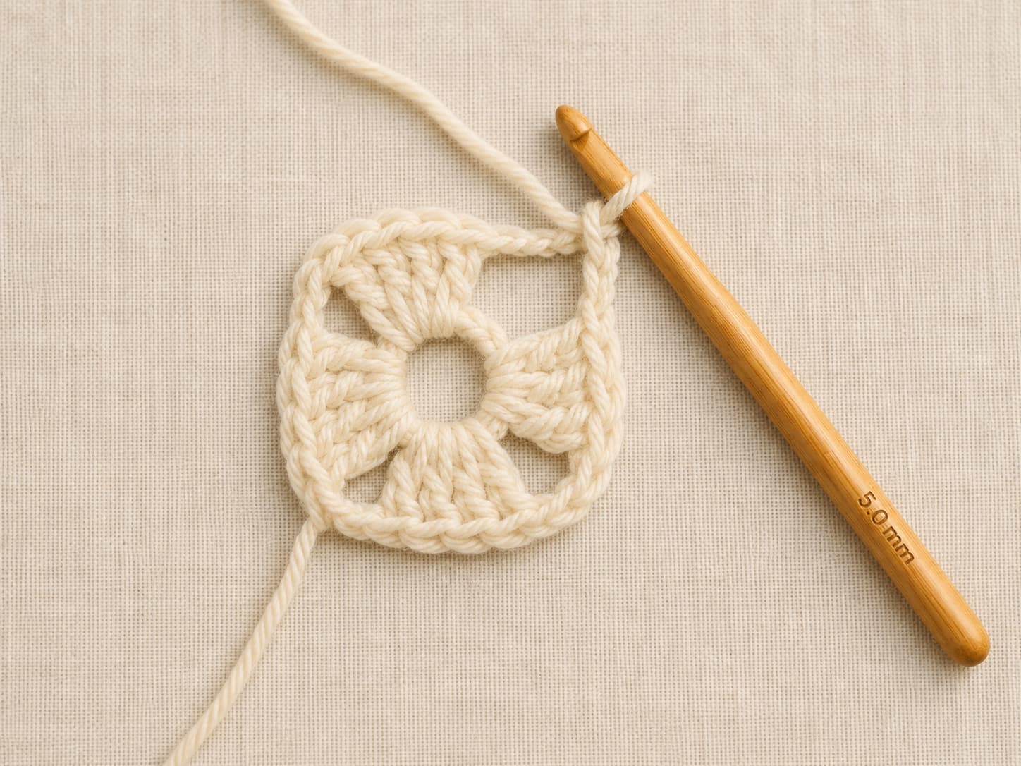Round one of a cream granny square in progress with three double-crochet clusters and an open fourth corner space.