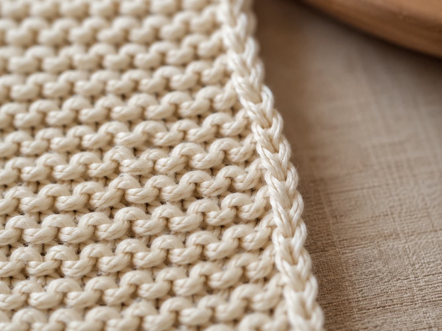 Close-up of the chain-like slipped-stitch edge along a cream garter-stitch scarf.