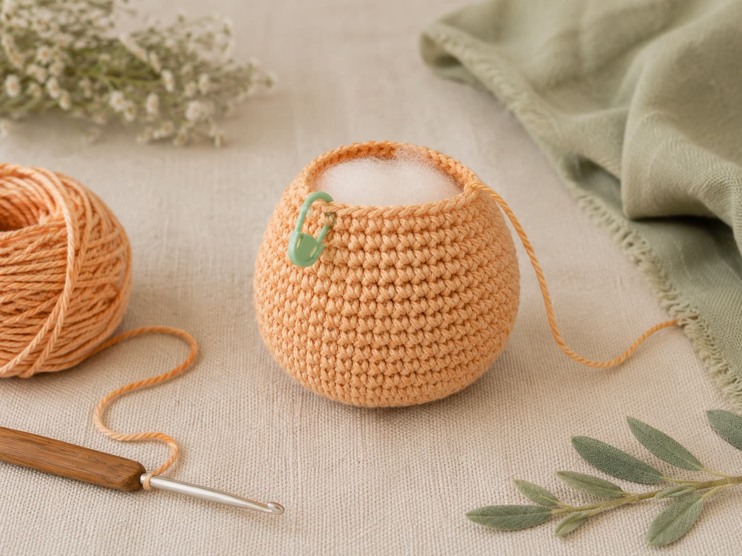 Apricot-ginger amigurumi cat body in progress with tight single crochet stitches, light stuffing, and a muted-sage stitch marker on warm ivory linen.