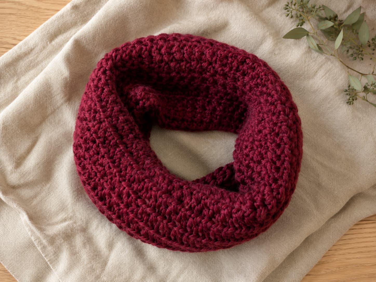 Finished deep cranberry crochet chunky cowl in bulky yarn arranged naturally on warm oatmeal linen.