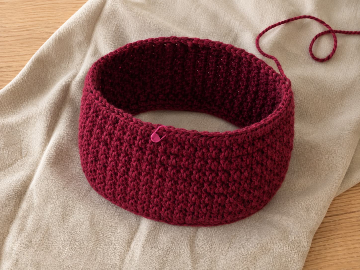 Deep cranberry chunky cowl in progress with several even joined rounds of half double crochet and a stitch marker at the round start.