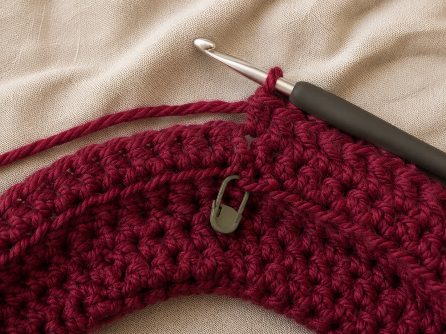 Close-up of the joined-round seam on a deep cranberry half double crochet cowl showing the slip stitch join and first stitch of the next round.