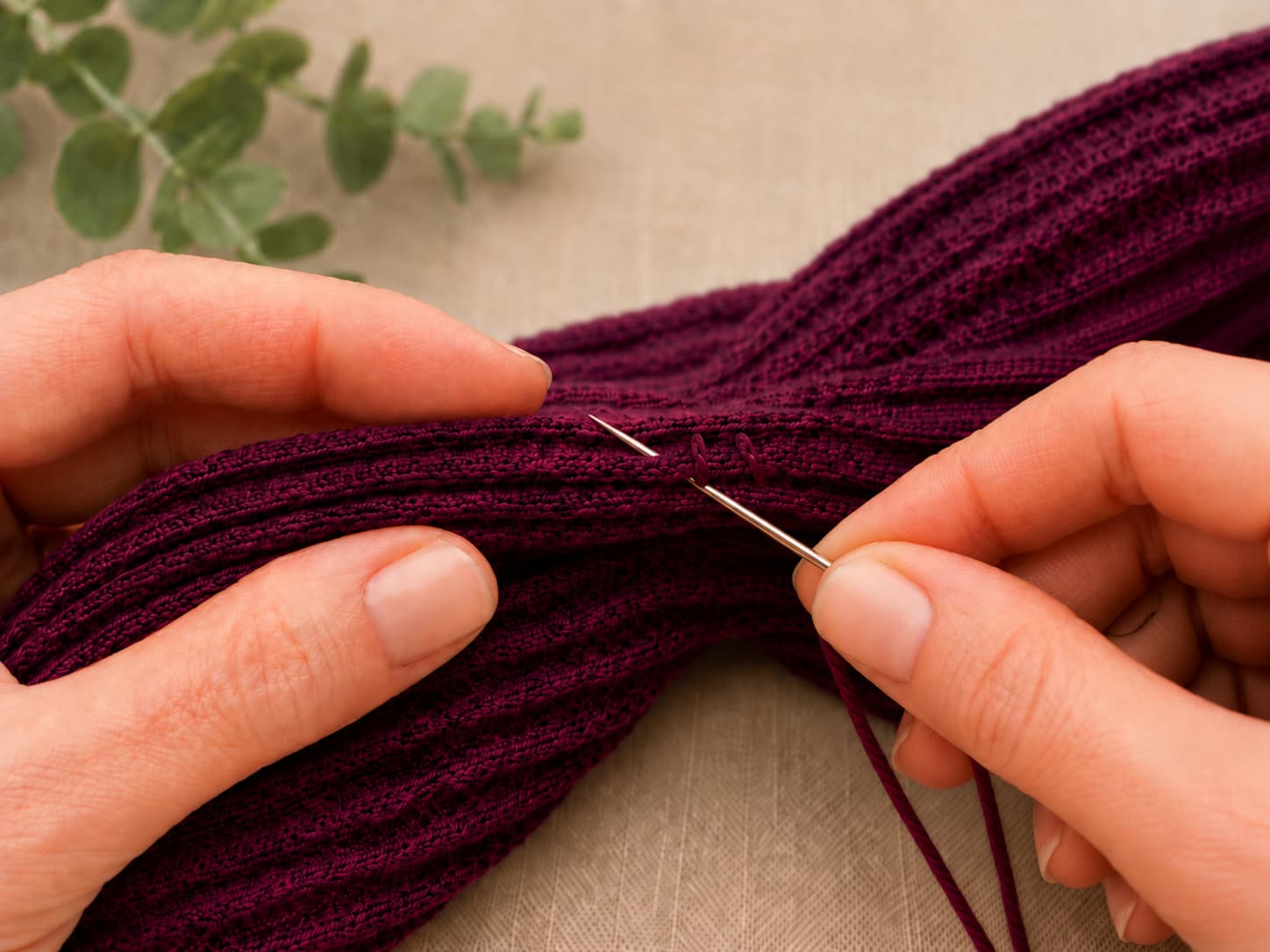 Close-up of a tapestry needle sewing through all four interlocked plum-berry crochet layers with an even whip stitch.