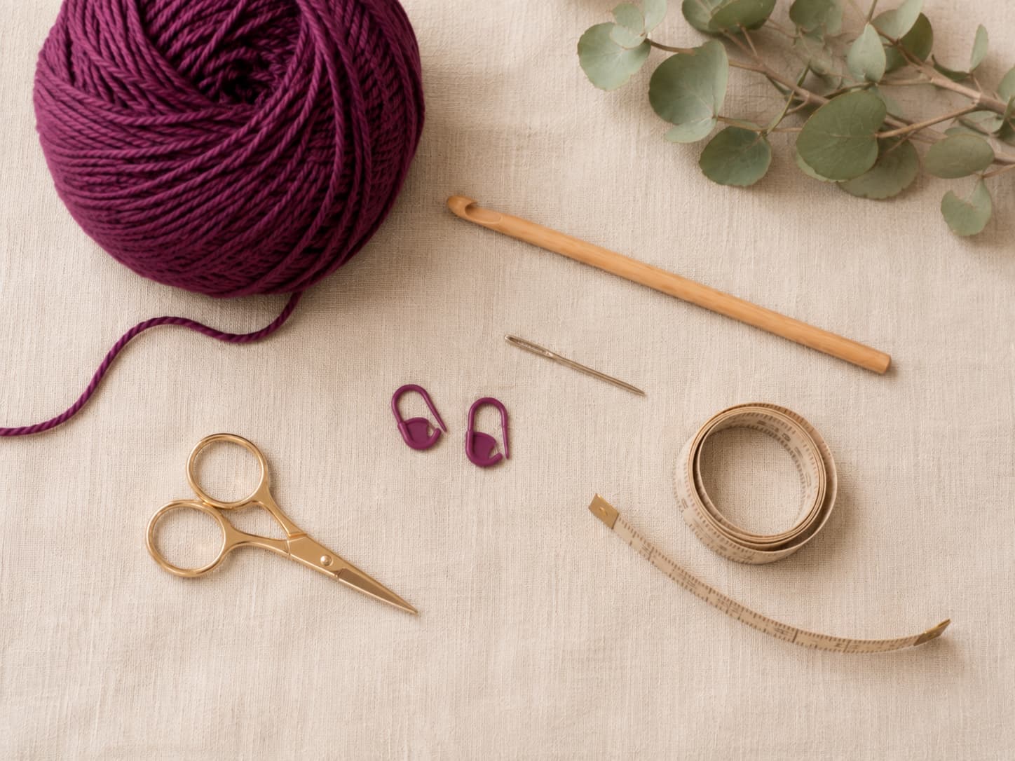 Soft plum-berry medium-weight yarn, a 5.0 mm crochet hook, tapestry needle, two stitch markers, scissors, and measuring tape arranged on warm oatmeal linen.