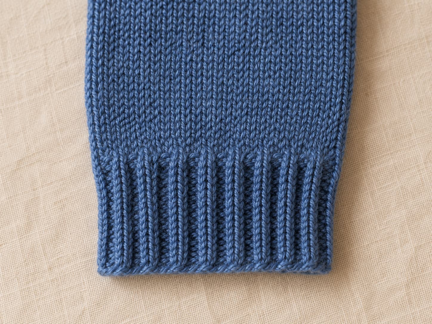 Close-up of a heathered denim fingerless mitt panel showing a stretchy 2x2 ribbed cuff transitioning into smooth stockinette knitting.