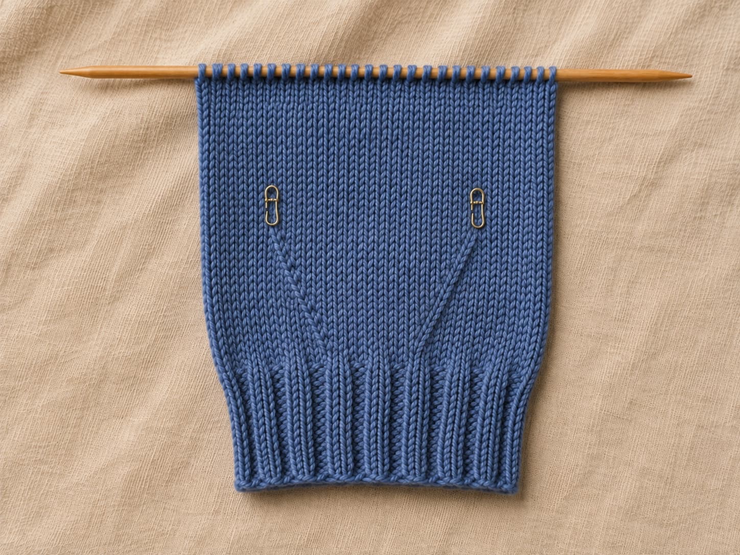 Flat fingerless mitt panel in heathered denim yarn with two stitch markers framing a widening thumb gusset formed by paired M1 increases.