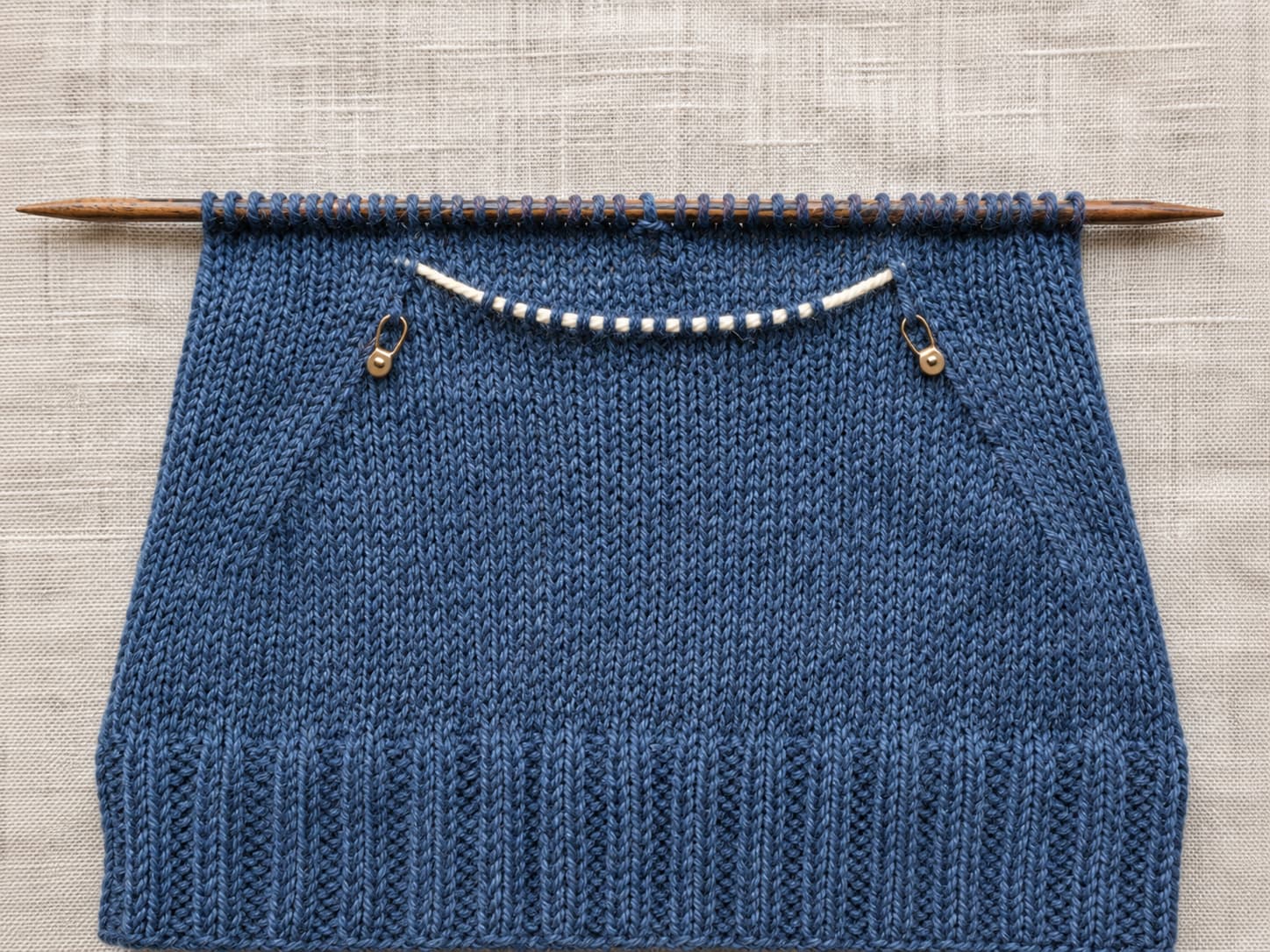Thirteen thumb-gusset stitches held on contrast waste yarn while the flat fingerless mitt hand continues above a one-stitch bridge.