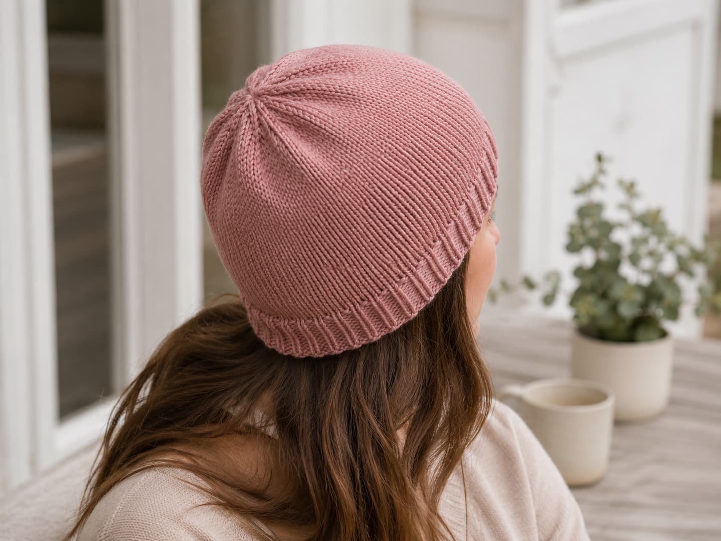 Dusty-rose stockinette beanie shown from the back and side, with a single-layer ribbed brim fitting closely around the head and a smooth rounded crown.
