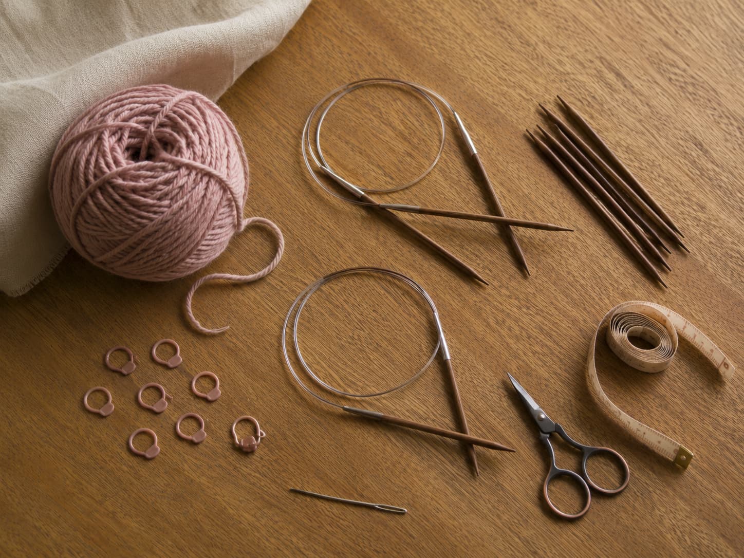 Dusty-rose smooth worsted-weight yarn, 4.5 mm and 5 mm circular needles, matching DPNs, stitch markers, measuring tape, scissors, and a tapestry needle arranged on natural linen.