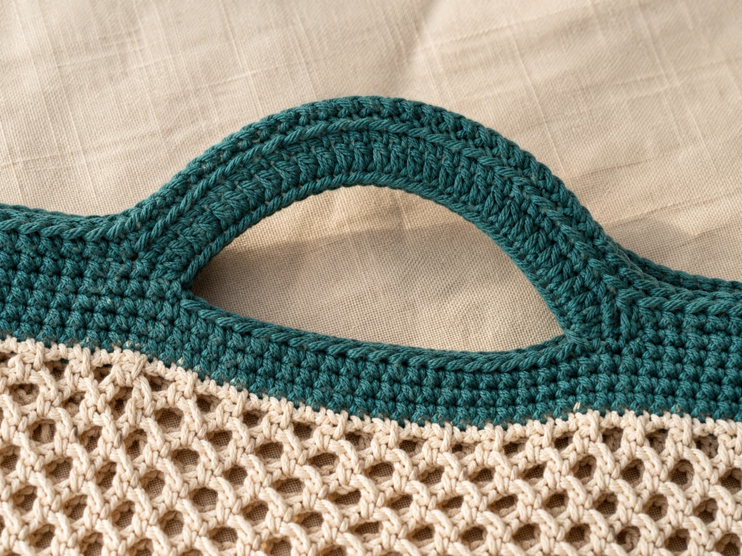 Close-up of a deep jade-teal integrated crochet handle with two single crochet reinforcement rounds and a centered surface slip-stitch ridge.