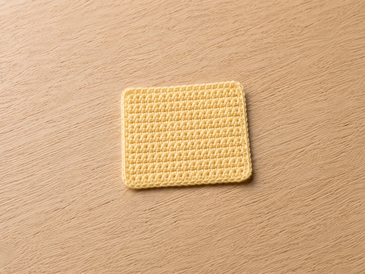 Warm-coral single crochet square coaster with sixteen even stitches across, straight side edges, and a dense washable fabric on warm off-white linen.
