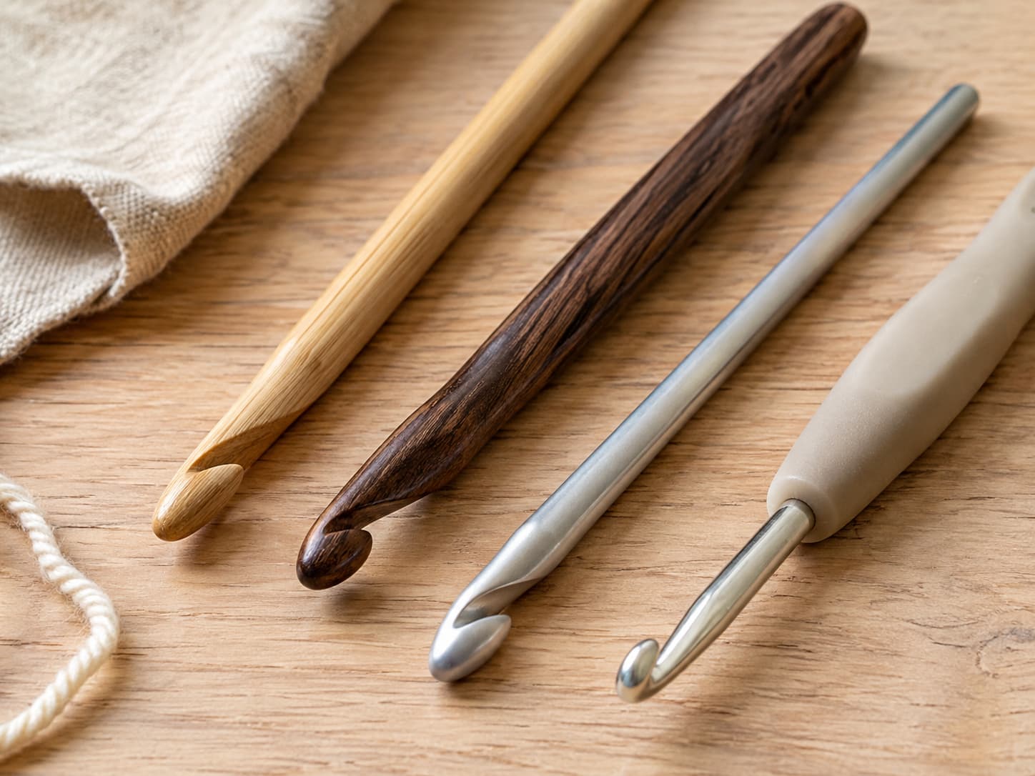 Aluminum inline and tapered crochet hooks beside bamboo and soft-grip ergonomic hooks on natural linen.