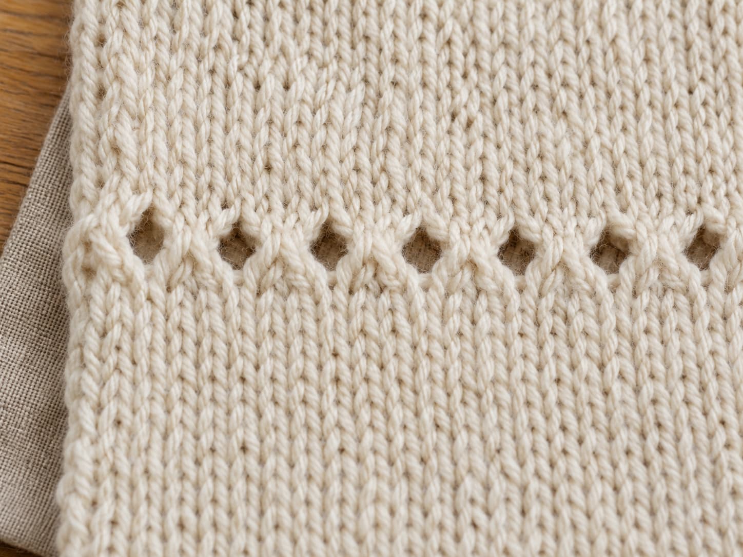 Detail of the Cloud Nine Stitch eyelet row showing yarn over holes and knit-two-together decreases in soft cream worsted yarn.
